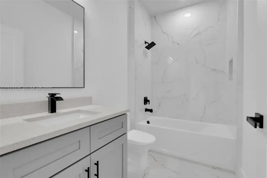 Guest bath with tub and shower combination, quartz-topped gray vanity, and black fixtures.