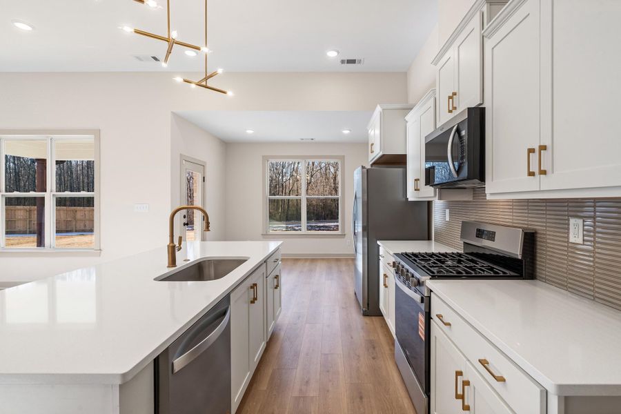 Kitchen with stainless steel appliances, white cabinetry, and an island with sink