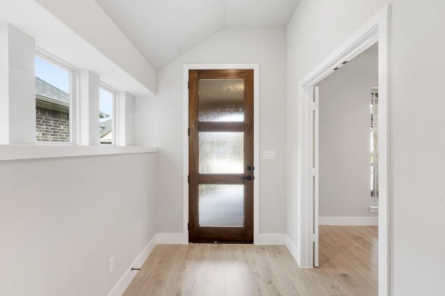 Entryway with dark wood door featuring frosted glass panels, vaulted ceiling, and light hardwood floors