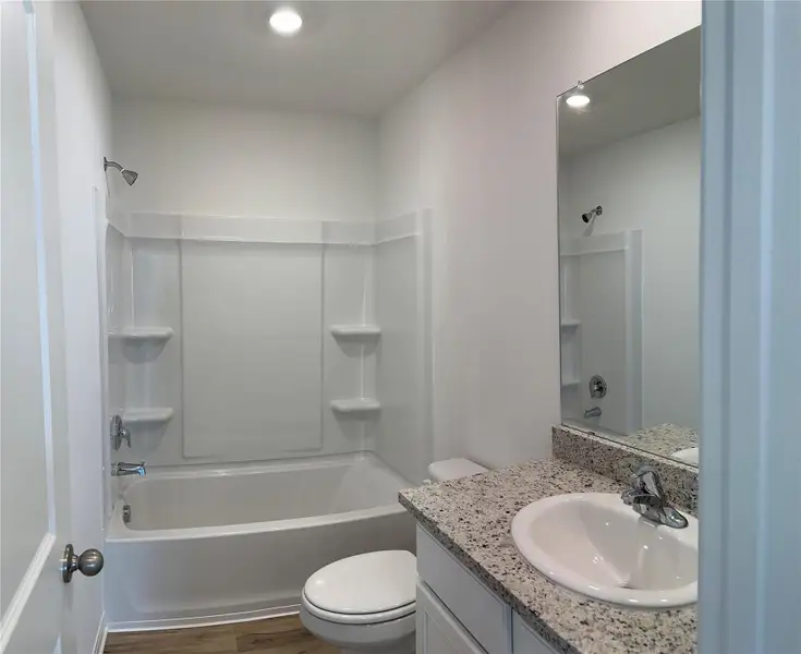 Secondary bathroom includes granite counters, designer white cabinetry and luxury vinyl plank flooring.