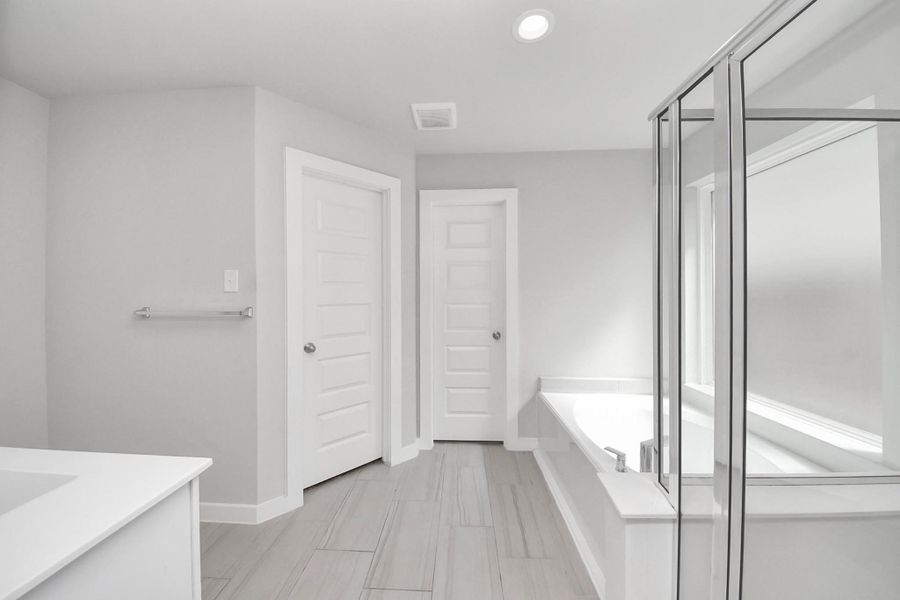 Large primary bathroom featuring a glass-enclosed walk-in shower, a relaxing soaking tub with a nearby window for natural light, and a clean modern layout that offers both comfort and functionality.