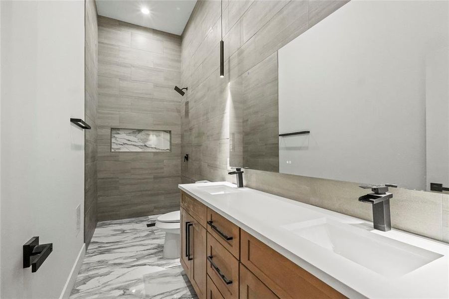 Bathroom with tiled shower, tile patterned flooring, toilet, and vanity