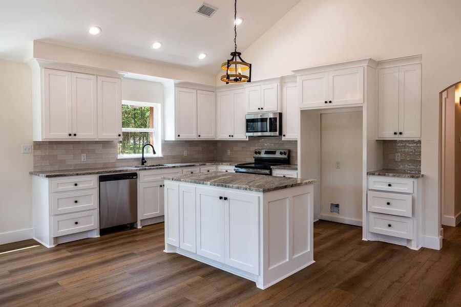 Kitchen featuring white cabinetry, stainless steel appliances, light stone countertops, backsplash, and high vaulted ceiling