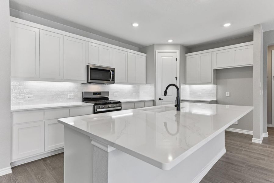 Kitchen featuring decorative backsplash, appliances with stainless steel finishes, an island with sink, light stone counters, and dark wood finished floors Kitchen featuring decorative backsplash, appliances with stainless steel finishes, an island with sink, light stone counters, and dark wood finished floors