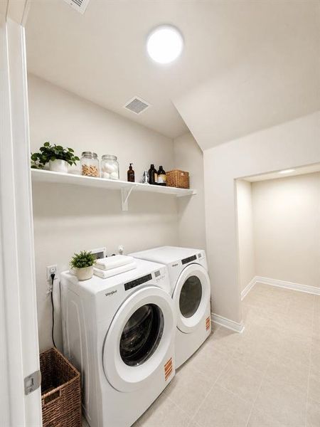 Dedicated laundry space featuring a white floating shelf, neutral wall tones, and light tile flooring