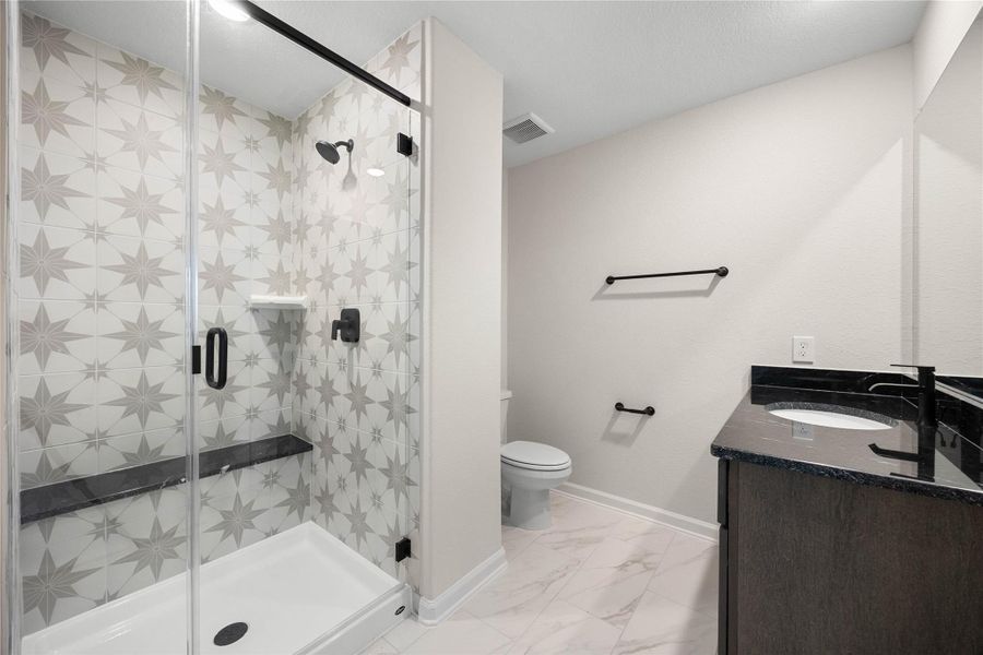Stylish private ensuite bathroom attached directly to the secondary bedroom. This beautifully upgraded space features a modern walk-in shower showcasing a striking starburst-patterned accent tile wall, a built-in granite bench ledge, and a seamless glass door enclosure. The matching dark vanity is topped with high-contrast black granite countertops and a contemporary matte black faucet, offering a cohesive, designer look for guests or family. Stylish private ensuite bathroom attached directly to the secondary bedroom. This beautifully upgraded space features a modern walk-in shower showcasing a striking starburst-patterned accent tile wall, a built-in granite bench ledge, and a seamless glass door enclosure. The matching dark vanity is topped with high-contrast black granite countertops and a contemporary matte black faucet, offering a cohesive, designer look for guests or family.