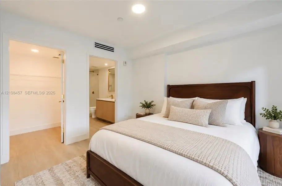 Neutral-toned wood-finish flooring, walk-in closet with built-in shelving, and bathroom featuring a light-finish wood vanity with a solid-surface countertop Neutral-toned wood-finish flooring, walk-in closet with built-in shelving, and bathroom featuring a light-finish wood vanity with a solid-surface countertop