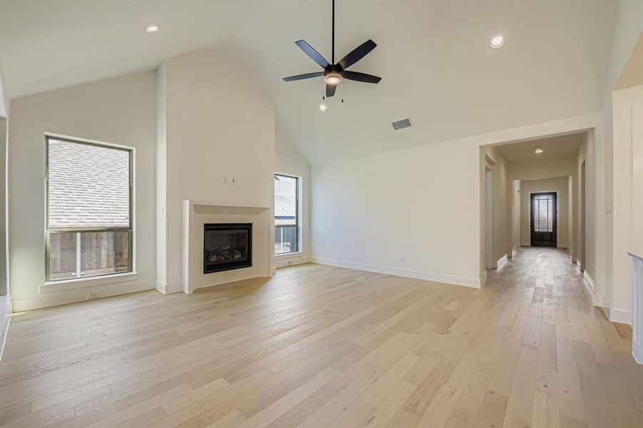Unfurnished living room with a high ceiling, a ceiling fan, light wood-style flooring, a glass covered fireplace, and recessed lighting