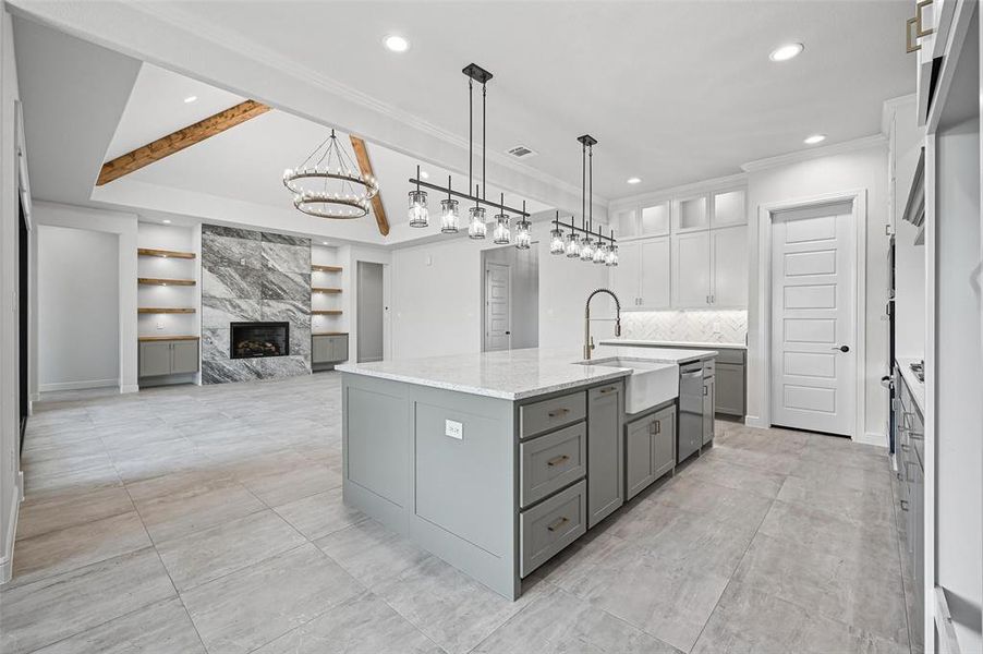 Kitchen featuring a high end fireplace, light stone countertops, open floor plan, an island with sink, and pendant lighting Kitchen featuring a high end fireplace, light stone countertops, open floor plan, an island with sink, and pendant lighting