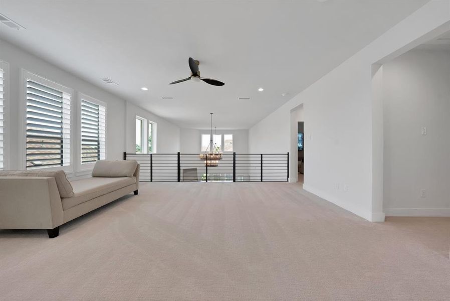 Spacious second-level landing featuring plush carpeting, multiple windows with louvered shutters, a contemporary ceiling fan, recessed lighting, and a modern horizontal railing overlooking the lower level Spacious second-level landing featuring plush carpeting, multiple windows with louvered shutters, a contemporary ceiling fan, recessed lighting, and a modern horizontal railing overlooking the lower level