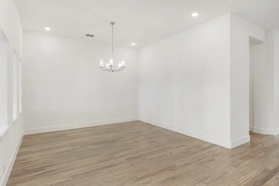 Empty dining room with wood-look floors, white walls, and a modern chandelier with candle-style lights Empty dining room with wood-look floors, white walls, and a modern chandelier with candle-style lights