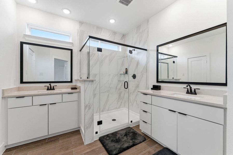 Luxurious primary bath with dual quartz vanities, large framed mirrors, and a walk-in glass shower.