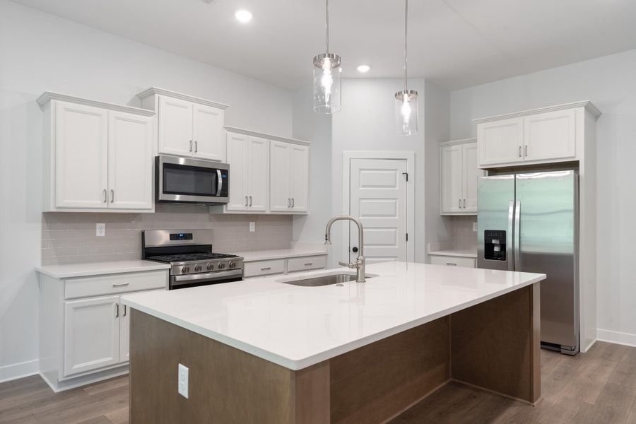 White cabinetry, stainless steel appliances, central island with sink, quartz countertops, and wood-finish flooring