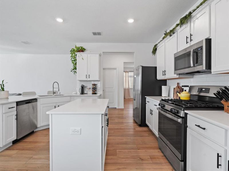 Kitchen featuring white cabinetry, sink, stainless steel appliances, tasteful backsplash, and light hardwood / wood-style floors