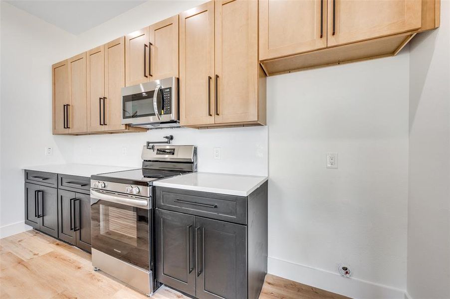 Kitchen with appliances with stainless steel finishes, light brown cabinetry, light wood-style flooring, and light stone countertops