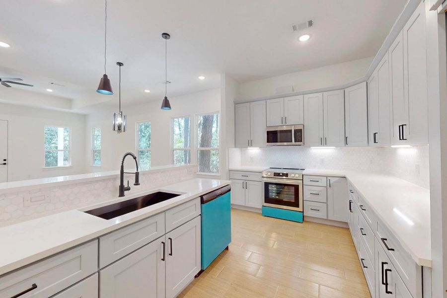 Kitchen with stainless steel appliances, decorative light fixtures, white cabinets, tasteful backsplash, and light stone counters
