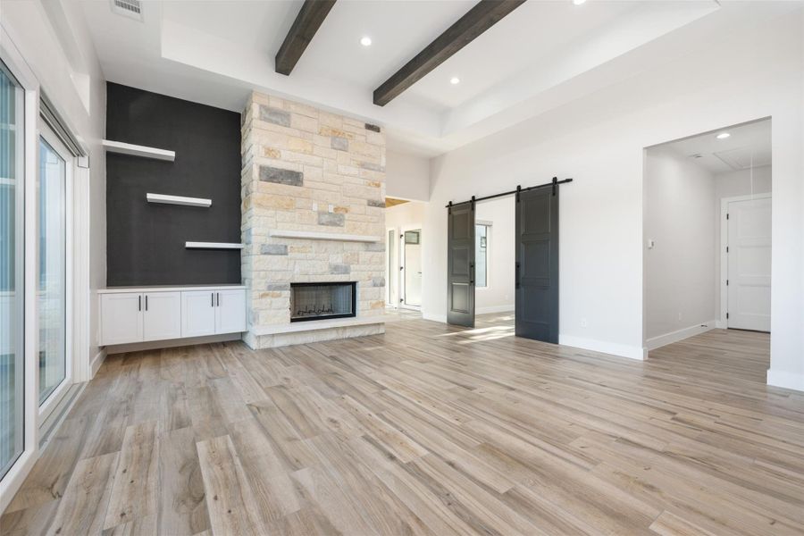 Unfurnished living room featuring a stone fireplace, a barn door, light hardwood / wood-style floors, and beamed ceiling