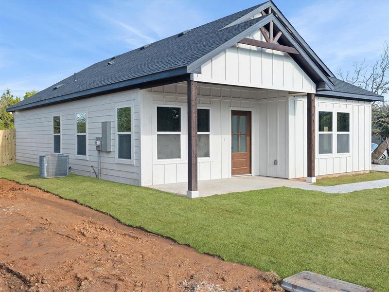 Front view of house with a shingled roof, board and batten siding, a yard, and a porch Front view of house with a shingled roof, board and batten siding, a yard, and a porch
