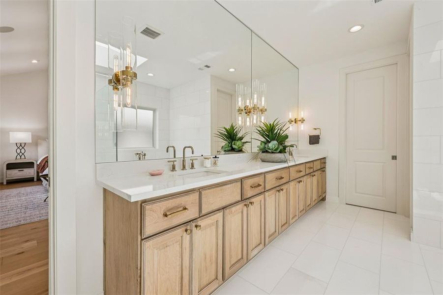 Expansive vanity featuring a quartz countertop, dual sinks with brass-finish fixtures, and extensive wood cabinetry with brass hardware