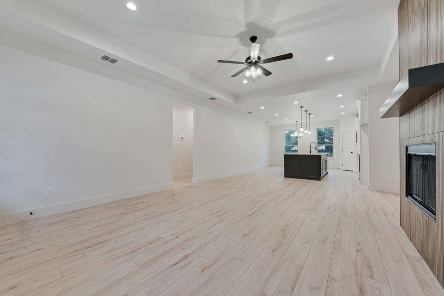 Unfurnished living room featuring a tray ceiling, a fireplace, recessed lighting, light wood-style flooring, and ceiling fan