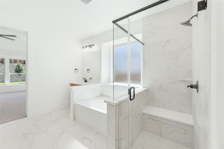 Master bathroom with marble tile, soaking tub, glass-enclosed walk-in shower with bench, and black fixtures Master bathroom with marble tile, soaking tub, glass-enclosed walk-in shower with bench, and black fixtures