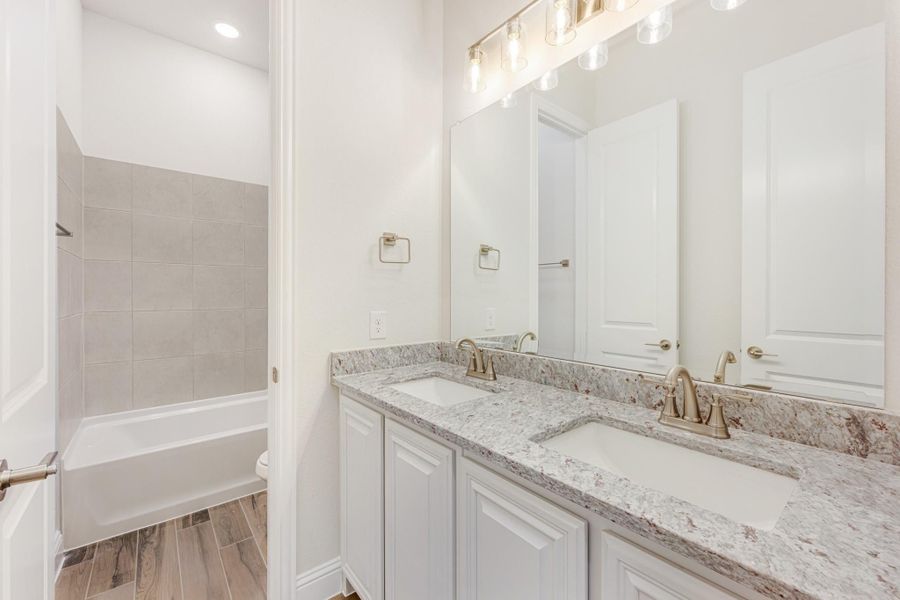Bathroom with double sink vanity, granite countertops, white cabinets, and tiled bathtub surround