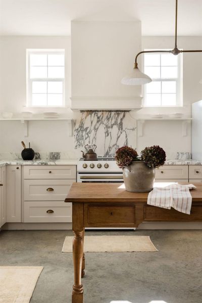 Kitchen with concrete floors, light stone counters, high end range, and white cabinetry