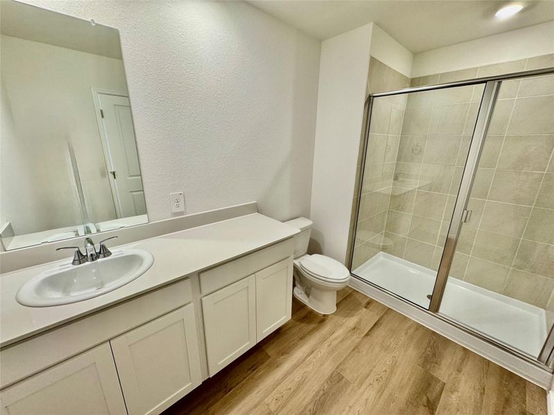 Full bathroom featuring vanity, a shower stall, light wood-style flooring, and a textured wall
