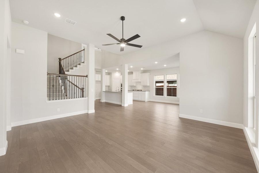 Open living area with hardwood floors, ceiling fan, and open-concept kitchen and staircase in background