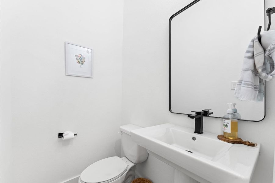 Chic and convenient, this first-floor powder room is thoughtfully positioned for guests and everyday ease. Featuring a stylish pedestal sink, cute lighting, and a statement mirror, the space blends function with flair.