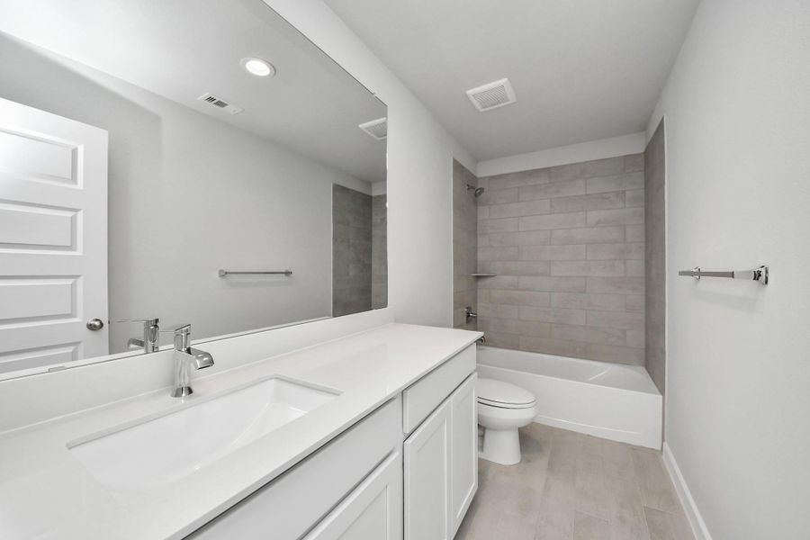 Secondary bath features tile flooring, bath/shower combo with tile surround, light stained wood cabinets, beautiful light countertop.