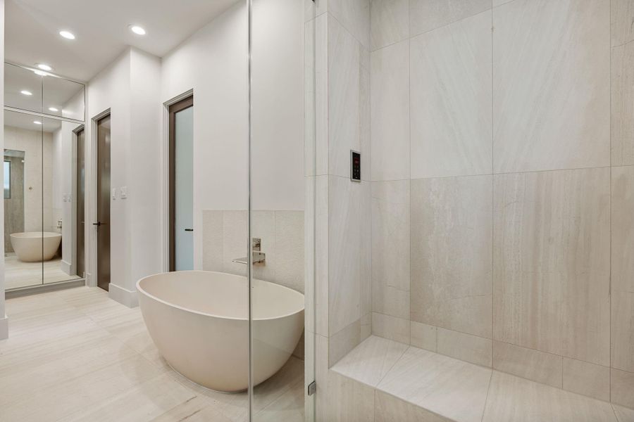 From the steam shower, complete with an integrated bench and steam controls, the space opens to a soaking tub accented in limestone and a full-height mirrored linen cabinet, discreetly concealing adjustable shelving behind seamless, operable fronts. From the steam shower, complete with an integrated bench and steam controls, the space opens to a soaking tub accented in limestone and a full-height mirrored linen cabinet, discreetly concealing adjustable shelving behind seamless, operable fronts.