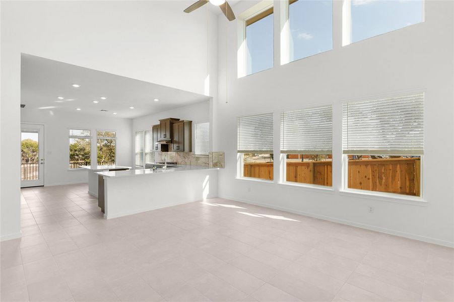 Unfurnished living room featuring a ceiling fan, baseboards, recessed lighting, and a high ceiling