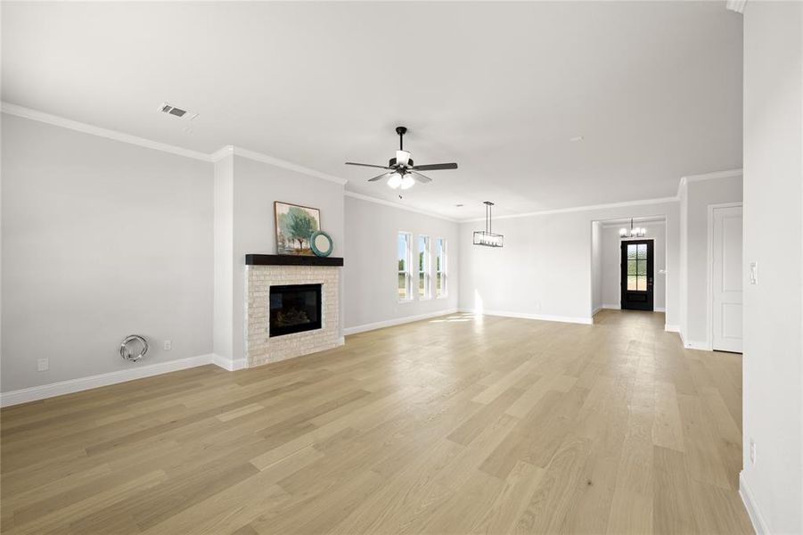 Unfurnished living room featuring a healthy amount of sunlight, light hardwood / wood-style floors, ceiling fan with notable chandelier, and a brick fireplace