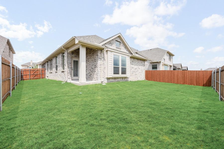 Brick home rear exterior with covered patio, large grassy backyard, and wood privacy fence