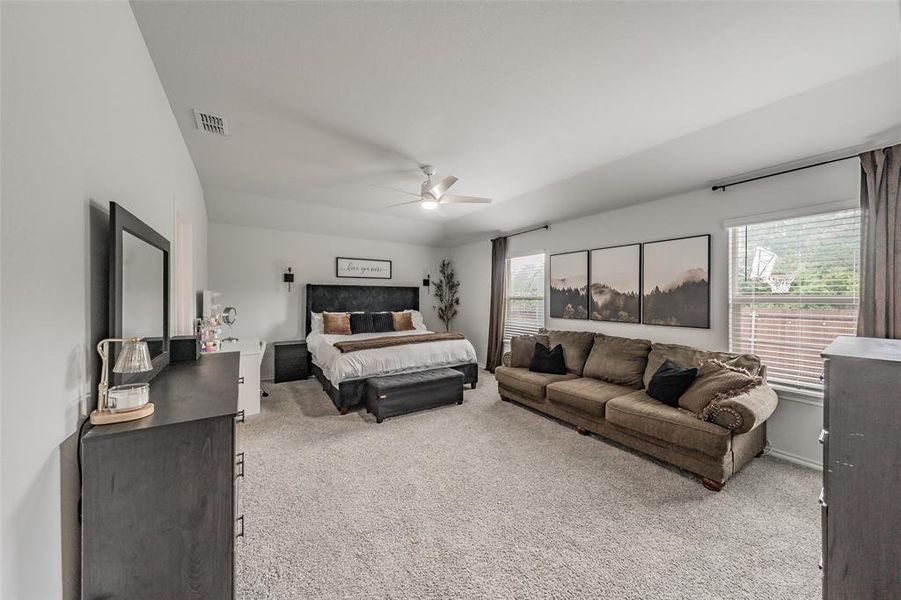 Spacious room featuring light-colored carpet flooring, multiple windows with blinds, and a ceiling fan