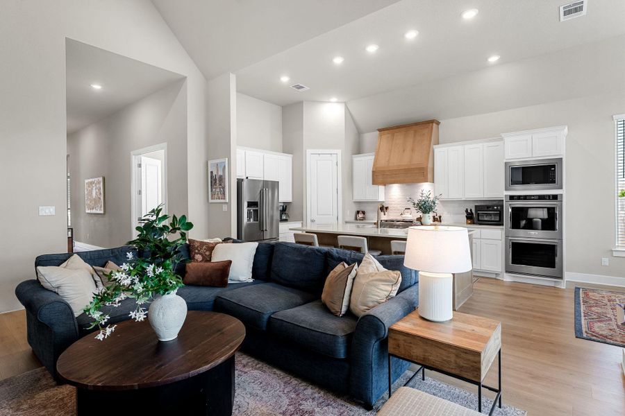 Combined living area and kitchen featuring vaulted ceilings, recessed lighting, and wood-finish flooring