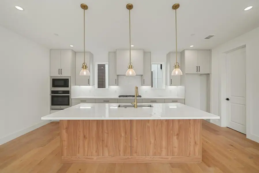 Kitchen featuring a wood-finish island with a white countertop, light gray cabinetry, built-in stainless steel appliances, and wood-finish flooring Kitchen featuring a wood-finish island with a white countertop, light gray cabinetry, built-in stainless steel appliances, and wood-finish flooring