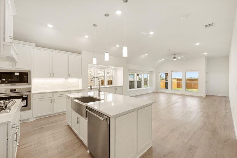 Open kitchen with white cabinets, center island, stainless appliances, and light wood floors opening to living area