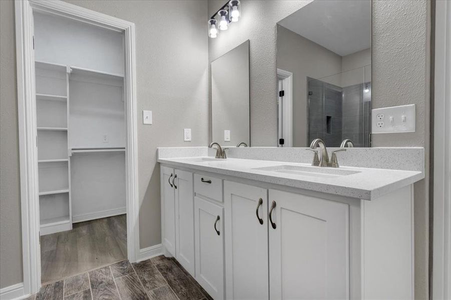 Full bathroom with wood finish floors, double vanity, a stall shower, a textured wall, and a spacious closet