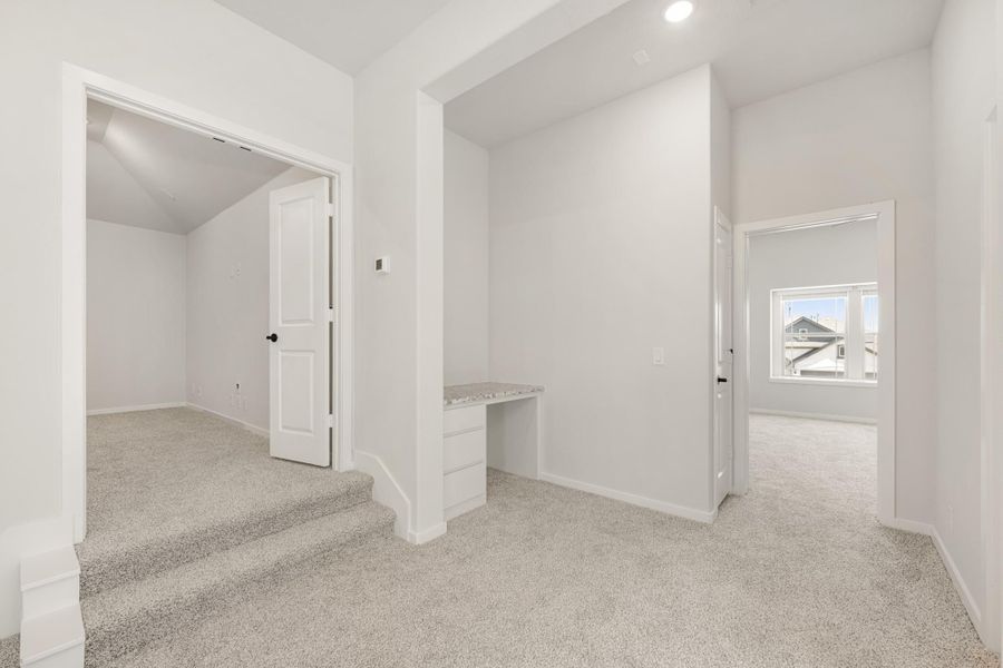 Upstairs hallway with carpet, built-in desk, and doors leading to multiple rooms