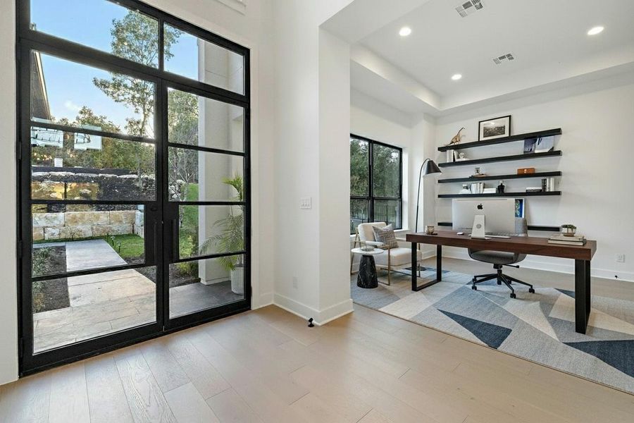 Light wood-finish flooring complements white walls and tall black-framed glass doors leading to exterior stone retaining walls