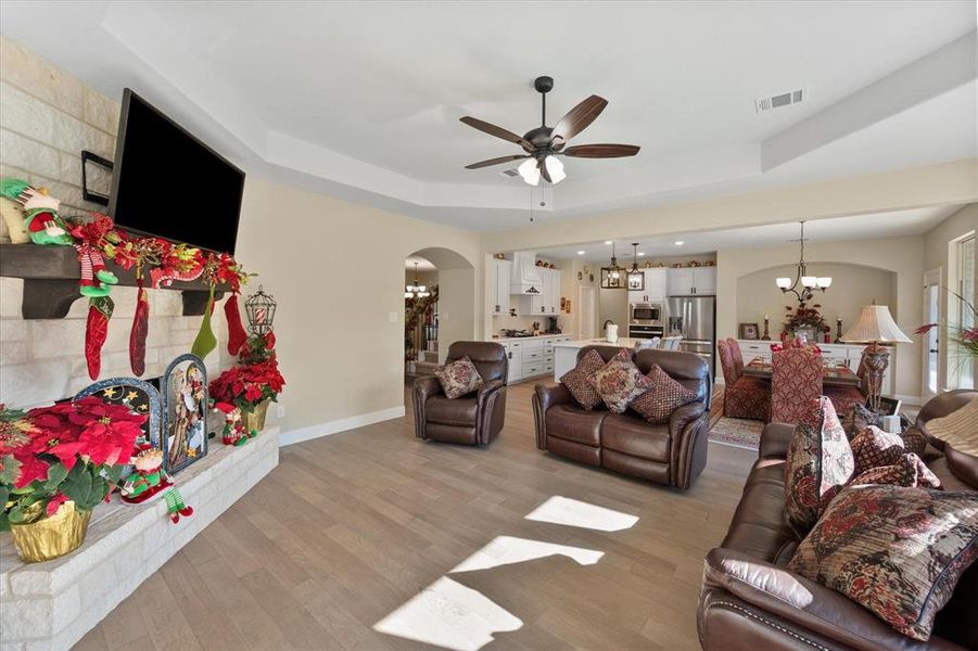 Living room featuring a chandelier, light wood finished floors, arched walkways, and a raised ceiling Living room featuring a chandelier, light wood finished floors, arched walkways, and a raised ceiling