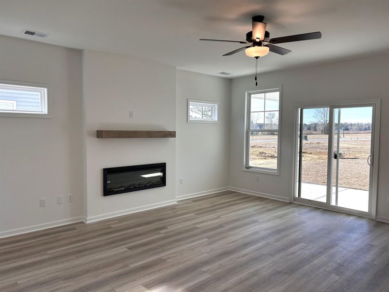 Unfurnished living room featuring a glass covered fireplace, wood finished floors, a ceiling fan, and plenty of natural light