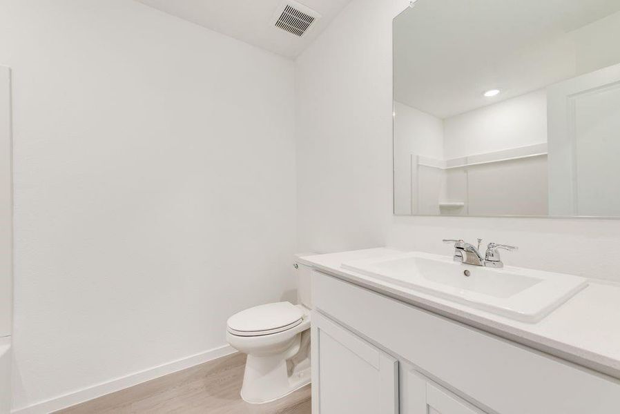 Full bathroom with toilet, wood finished floors, vanity, visible vents, and baseboards