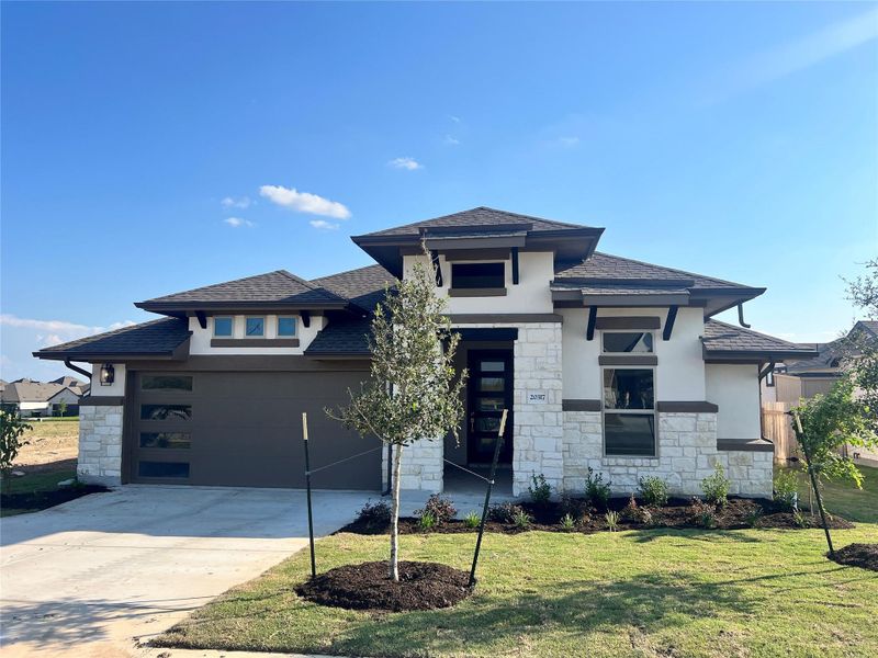 Prairie-style house featuring stucco siding, stone siding, a garage, and concrete driveway