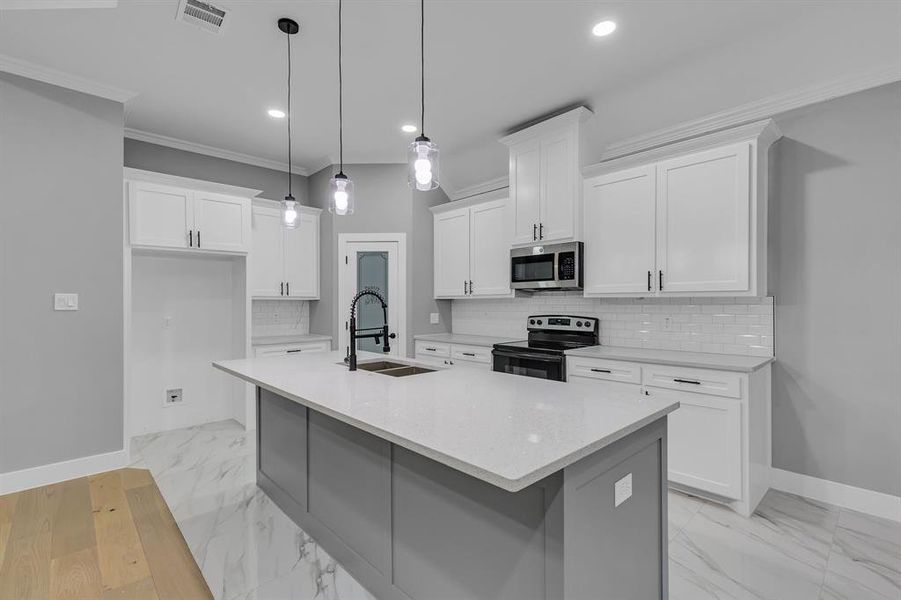 Kitchen with pendant lighting, a center island with sink, sink, appliances with stainless steel finishes, and white cabinetry