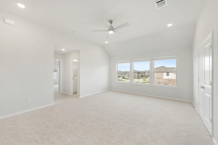 Spacious bedroom with vaulted ceiling, ceiling fan, carpet flooring, and large windows overlooking neighborhood