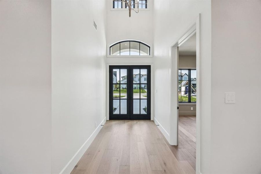 Entrance foyer with french doors, light wood-style flooring, and a high ceiling Entrance foyer with french doors, light wood-style flooring, and a high ceiling
