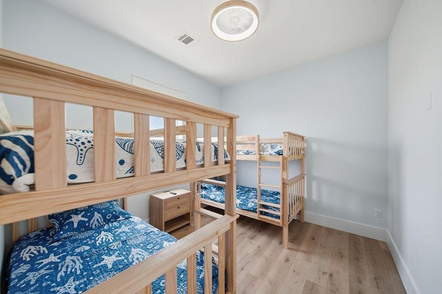This bedroom features two wooden bunk beds with ocean-themed bedding, light walls, hardwood floors, and a ceiling light fixture, creating a cozy and inviting space.